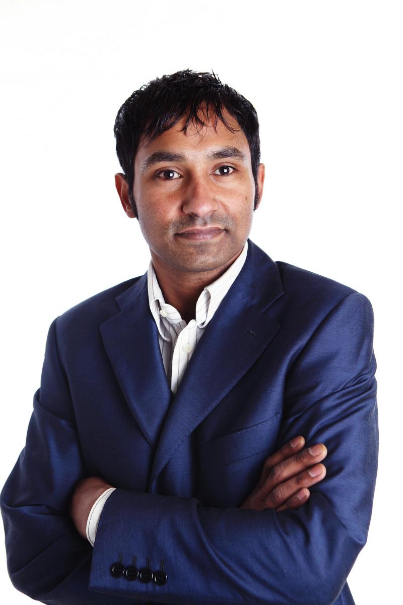 Parminder Singh Thandi in his navy suit and open shirt, with his arms folded.
